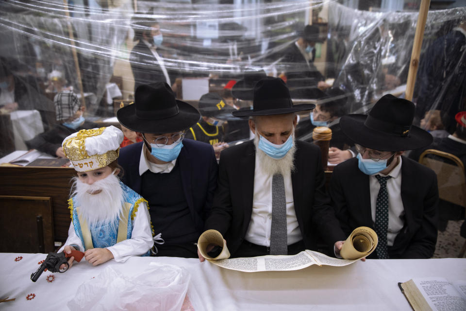 Jewish Ultra-Orthodox men and children, some wearing costumes and protective face masks, read the Book of Esther, which tells the story of the Jewish festival of Purim, at a synagogue separated by plastic partitions, follow new government measures to help stop the spread of the coronavirus, in Bnei Brak, Israel, Thursday, Feb 25, 2021. The Jewish holiday of Purim commemorates the Jews' salvation from genocide in ancient Persia, as recounted in the Book of Esther. (AP Photo/Oded Balilty)