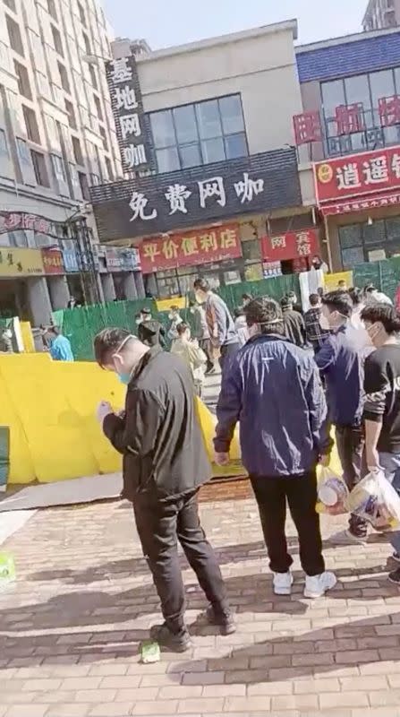 A group of people cross a downed fence following a protest at Foxconn's plant in Zhengzhou