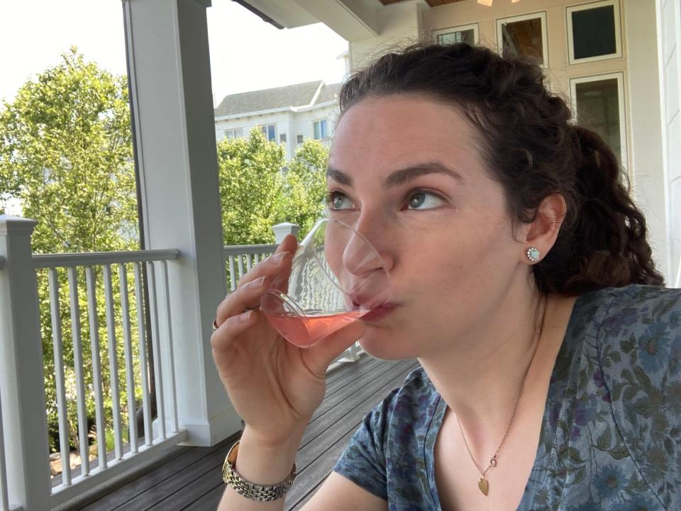 Insider reporter Talia Lakritz, who has brown curly hair and wears a blue shirt, sips pink lemonade on the porch at Dollywood's DreamMore Resort.