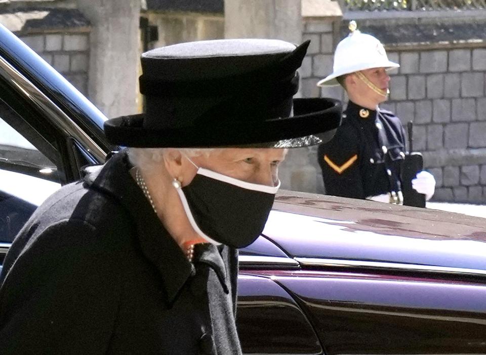 Queen Elizabeth II next to a car at Windsor Castle while a military member stands nearby.