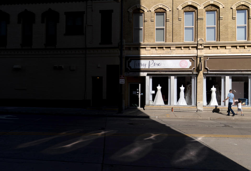 A father and son walk past a wedding gown shop in Appleton, Wis., Aug. 19, 2020. The downtown had been evolving as young parents moved back to Wisconsin from Minneapolis and Chicago, just to raise kids and open a business. Restaurants and boutiques popped up along College Avenue, catering to the professors and students at Lawrence University. Then the pandemic struck. (AP Photo/David Goldman)