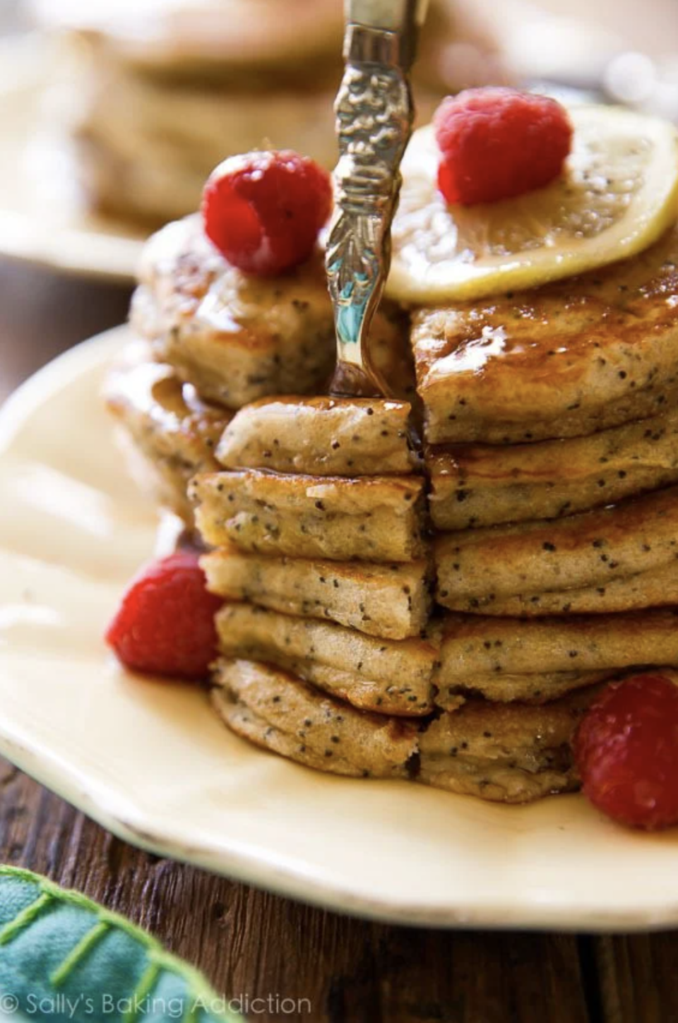 A stack of lemon poppy seed pancakes topped with lemon slices and raspberries, with a fork inserted
