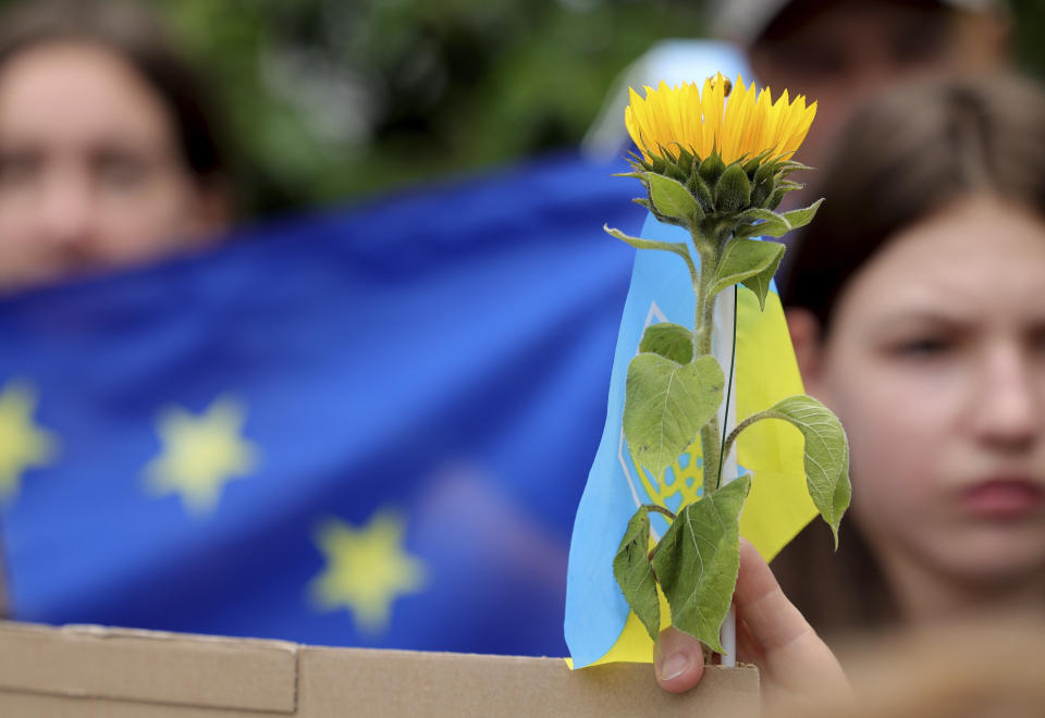 A protestor holds a yellow flower in front of an EU flag during a demonstration in support of Ukraine outside of an EU summit in Brussels, Thursday, June 23, 2022. European Union leaders are expected to approve Thursday a proposal to grant Ukraine a EU candidate status, a first step on the long toward membership. (AP Photo/Olivier Matthys)