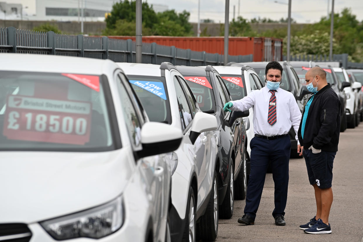 A car salesman (L) wearing PPE (personal protective equipment) including a face mask as a precautionary measure against COVID-19, shows customers vechiles parked on the forecourt of a recently re-opened Vauxhall car dealership in north London on June 4, 2020, as lockdown restrictions are eased during the noel coronavirus COVID-19 pandemic. - Car showrooms in England reopened this week as the UK government eased COVID-19 lockdown measures that have slammed the brakes on the industry. (Photo by JUSTIN TALLIS / AFP) (Photo by JUSTIN TALLIS/AFP via Getty Images)