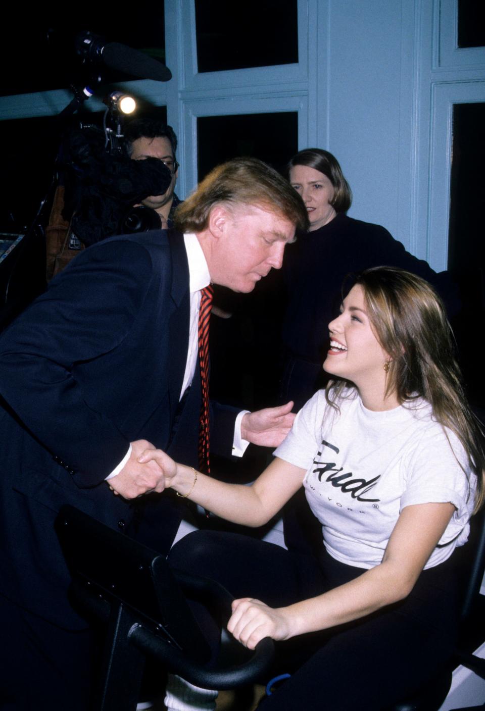 Donald Trump shakes hands with Alicia Machado as she sits on an exercise machine.