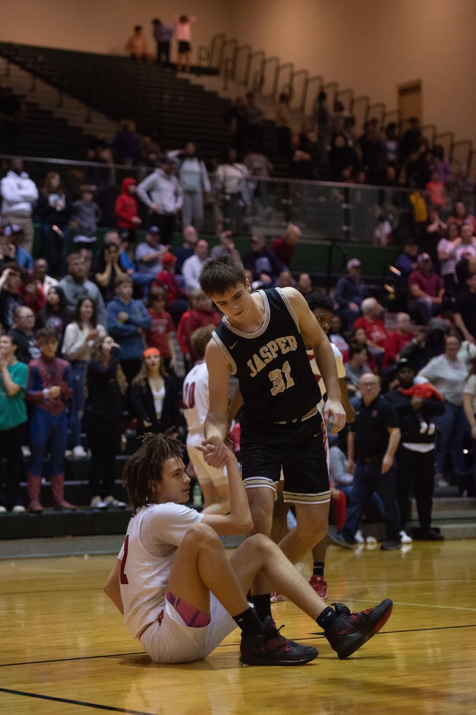 Jasper’s Andrew Noblitt (31) assists Harrison’s Jesiah Sloss (22) back to his feet after falling on the court during their game at North High School in Evansville, Ind., on Tuesday, Feb. 28, 2023.