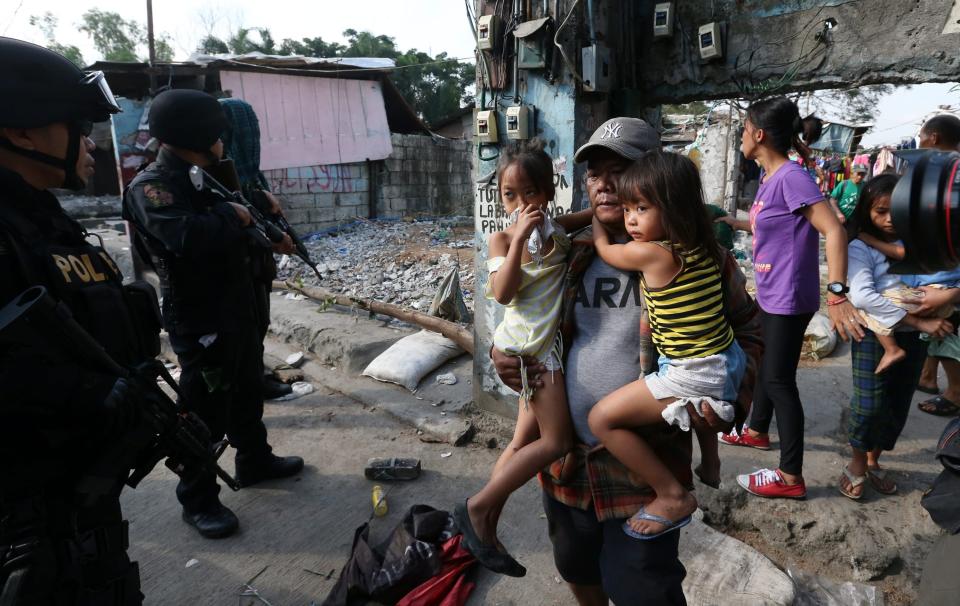 epa04044208 A Filipino father carries his daughters as policemen from the Special Weapons And Tactics (SWAT) team secure the area during a demolition of shanties at Sitio San Roque in Quezon City, east of Manila, Philippines, 27 January 2014. Throwing rocks, pillboxes, and even human waste, illegal settlers barricaded the demolition team in Baranggay Bagong Pag-asa. Four residents were arrested and twelve were reported injured. Residents report receiving cash from 300 to 450 US dollar in exchange for their voluntary relocation. Earlier, hundreds of the urban poor marched to the city hall in protest of the demolition that will pave the way for the rise of a business district. EPA/DENNIS M. SABANGAN