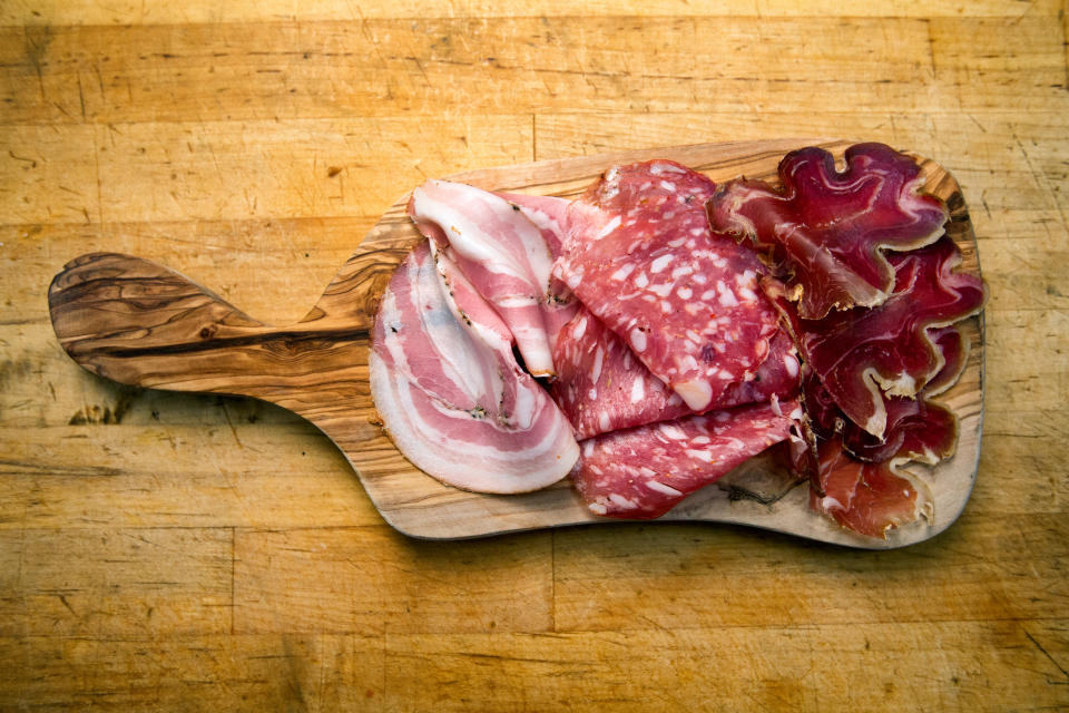 Delicious cuts of dried meat products, ham or bacon, salami and prosciutto on a rustic cutting board.