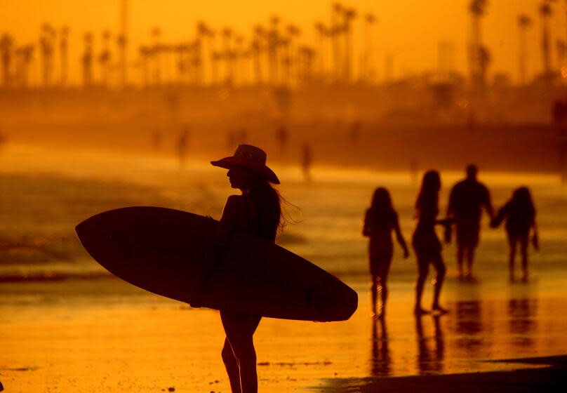 HUNTINGTON BEACH, CALIF. - JULY 12, 2023. Beachgoers take in the cooling mist of the ocean as the sun sets on Huntington Beach. Southern California weather is expected to get hotter in coming days as the region experiences the first significant heatwave of the summer. . (Luis Sinco / Los Angeles Times)