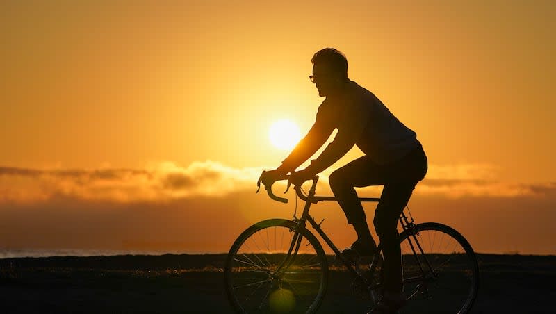 A bicyclist rides on a trail alongside the beach in Alameda, Calif., as the sun sets behind fog covering San Francisco, Thursday, Oct. 13, 2022.