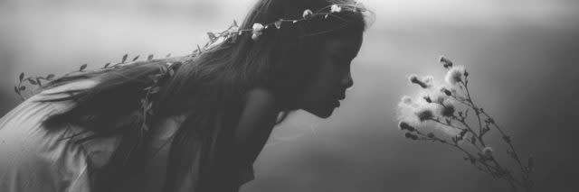 A young girl wearing a flower crown leaning over the smell a flower