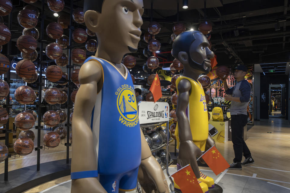 In this Friday, Oct. 11, 2019, photo, a shopper reach holds a basketball near statues of NBA players Stephen Curry of the Golden State Warriors, left, and Lebron James of the Los Angeles Lakers holding Chinese flags in the entrance of an NBA merchandise store Beijing. When Houston Rockets' general manager Daryl Morey tweeted last week in support of anti-government protests in Hong Kong, everything changed for NBA fans in China. A new chant flooded Chinese sports forums: "I can live without basketball, but I can't live without my motherland." (AP Photo/Ng Han Guan)