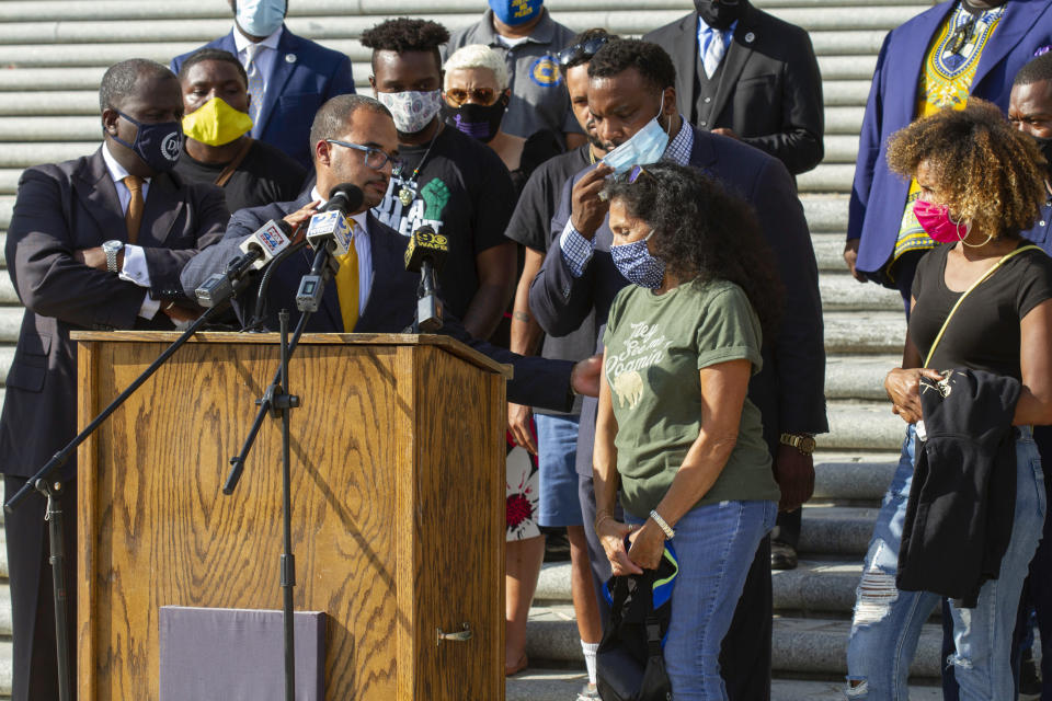 Attorney Ron Haley adjusts the microphone at the podium for Mona Hardin, center, mother of Ronald Greene, as she approaches to speak at a news conference outside the Louisiana State Capitol in Baton Rouge, La., Wednesday, Oct. 7, 2020. Attorney Lee Merritt stands directly behind Hardin. Greene died following a police chase in Louisiana in 2019, and his death is now under federal investigation. Greene's family filed a federal wrongful-death lawsuit in May alleging troopers "brutalized" Greene, used a stun gun on him three times and "left him beaten, bloodied and in cardiac arrest," before covering up his actual cause of death. (AP Photo/Dorthy Ray)