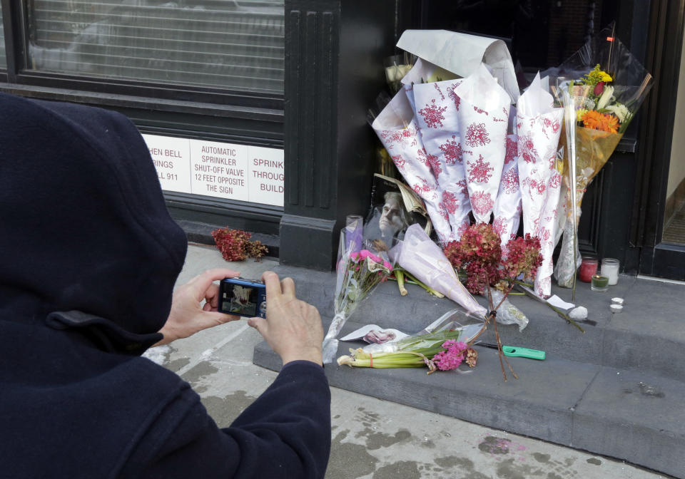 A passerby photographs the flowers placed outside the apartment building of actor Phillip Seymour Hoffman, in New York, Tuesday, Feb. 4, 2014. Autopsy results are expected soon in the death of actor Phillip Seymour Hoffman but police say it may take longer to determine if the heroin found in his apartment contains additives designed intensify the high. (AP Photo/Richard Drew)