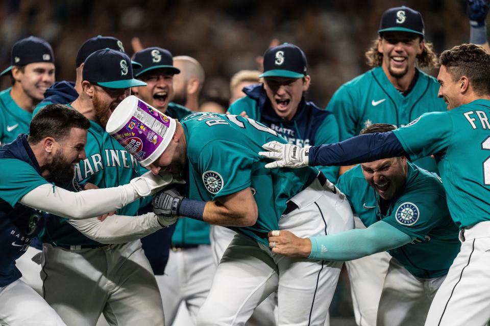 Seattle Mariners including Jesse Winker, left; Ty France, third from right; Logan Gilbert, second from right; and Adam Frazier, right celebrate a home run by Cal Raleigh in ninth inning of a baseball game against the Oakland Athletics, Friday, Sept. 30, 2022, in Seattle. The Mariners won 2-1 to clinch a spot in the playoffs. (AP Photo/Stephen Brashear)