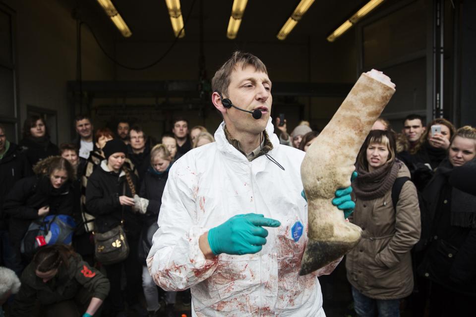 People look on as a veterinarian holds a leg of the giraffe Marius while it was being dismembered in Copenhagen Zoo