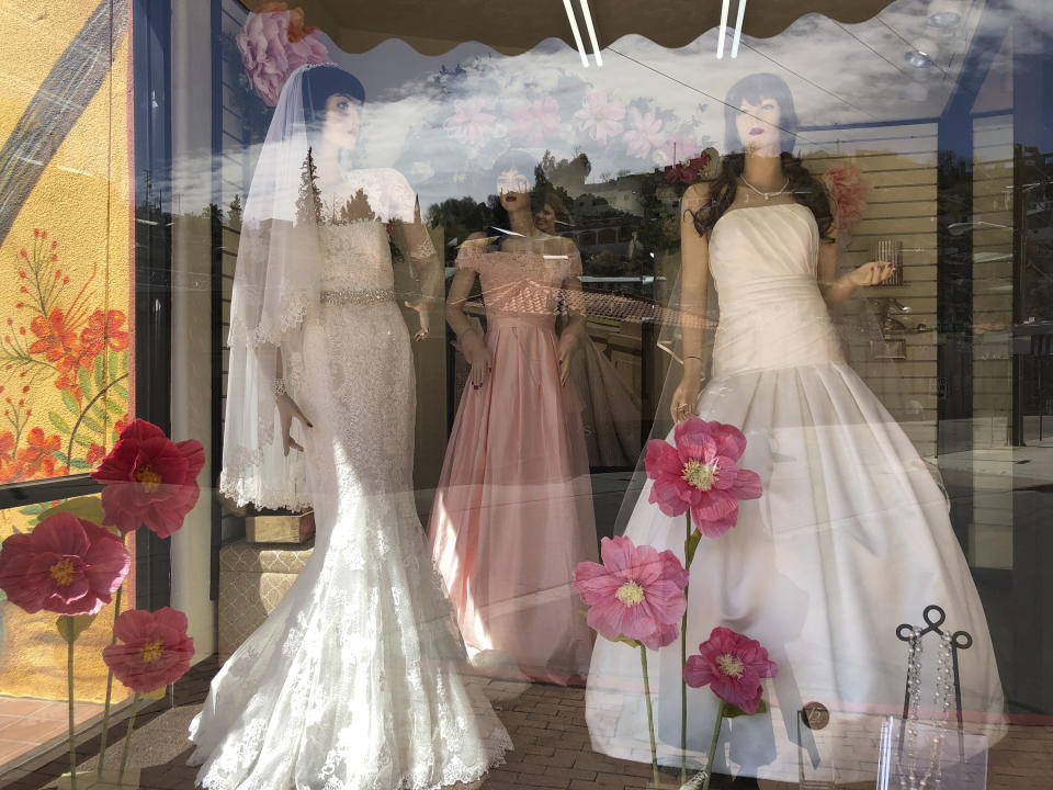 Mannequins in wedding gowns are seen in a window display on March 15, 2021, at a bridal store in Nogales, Ariz., that has been closed for nearly a year because of the pandemic. Like other border businesses, the store closed after its main customer base, Mexican day-trippers, were largely unable to come to the U.S. and shop after the U.S. partially closed its borders with Mexico and Canada in March 2020. (AP Photo/Suman Naishadham)