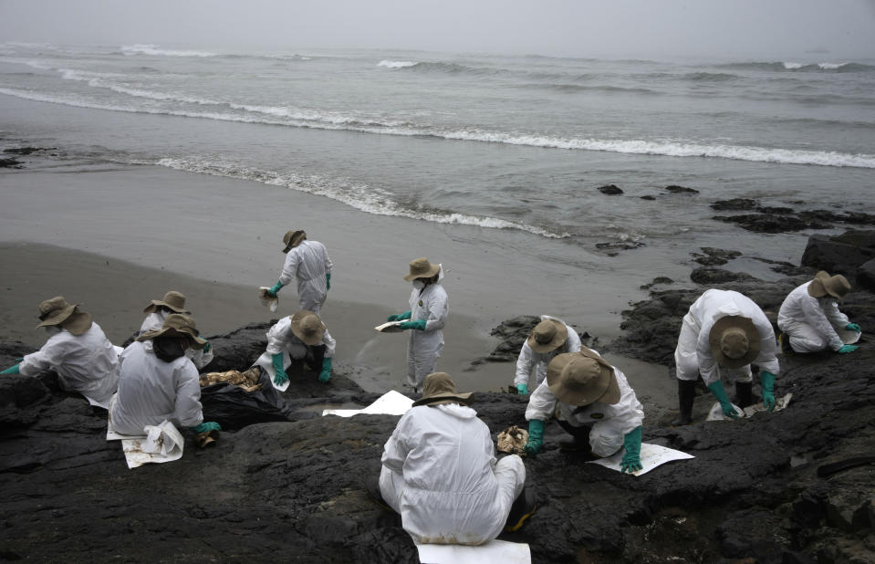 Workers clean oil on Cavero Beach in the Ventanilla district of Callao, Peru, Saturday, Jan. 22, 2022. The oil spill on the Peruvian coast was caused by the waves from an eruption of an undersea volcano in the South Pacific nation of Tonga. (AP Photo/Martin Mejia)