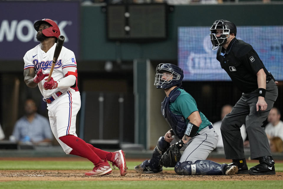 Texas Rangers' Adolis Garcia, left, Seattle Mariners catcher Tom Murphy, center, and umpire Mike Estabrook, right, watch a run-scoring single by Garcia that scored Marcus Semien in the fourth inning of a baseball game, Saturday, June 3, 2023, in Arlington, Texas. (AP Photo/Tony Gutierrez)