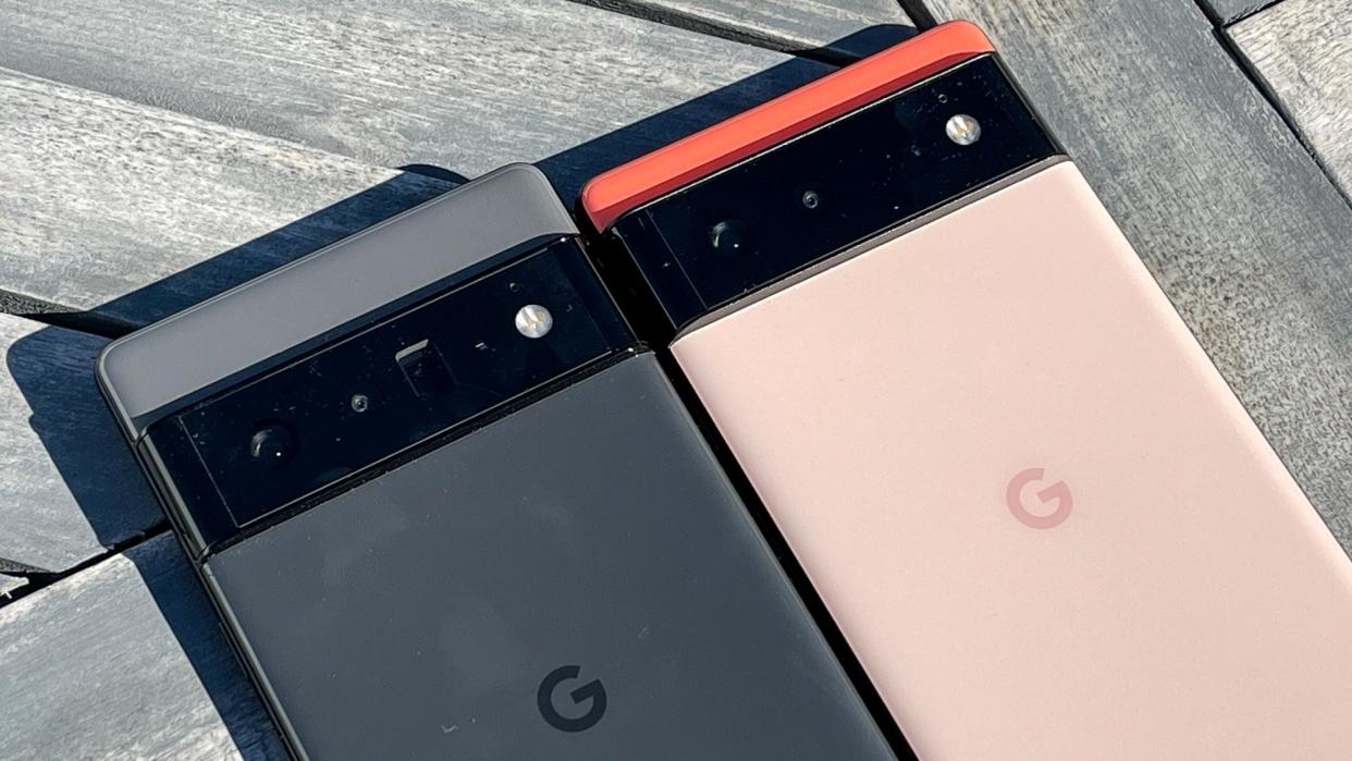  The Google Pixel 6 Pro (in black) and Google Pixel 6 (in coral) laid next to each other on wooden decking. 
