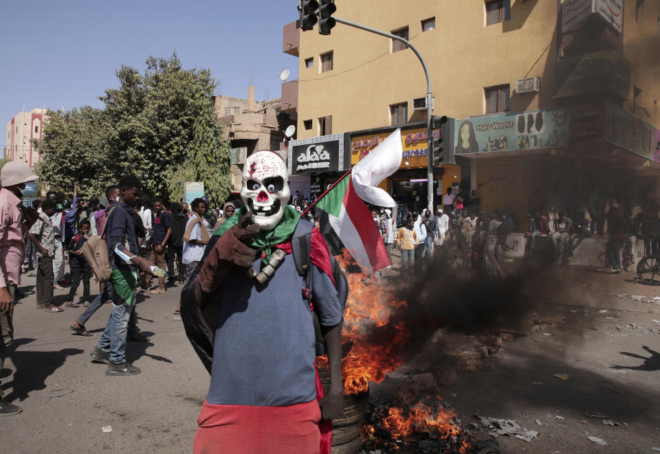 A masked demonstrator stands in front of burning tires during a protest to denounce the October 2021 military coup, in Khartoum, Sudan, Tuesday, Jan. 4, 2022. Sudanese took to the streets in the capital, Khartoum, and other cities on Tuesday in anti-coup protests as the country plunged further into turmoil following the resignation of the prime minister earlier this week. (AP Photo/Marwan Ali)