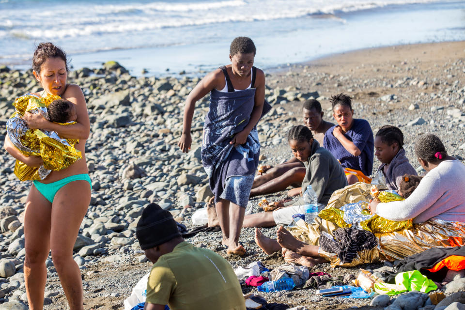 A migrant child is held by a beachgoer.