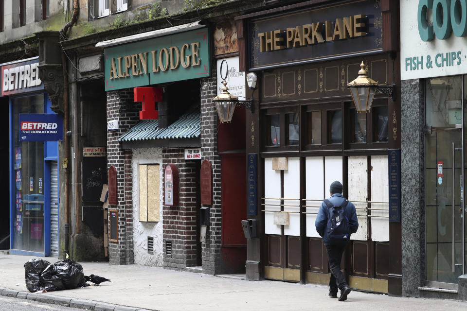 A man walks by boarded up bars as the UK continues its lockdown to help curb the spread of the coronavirus, in Glasgow, Scotland, Wednesday April 1, 2020. (Andrew Milligan/PA via AP)