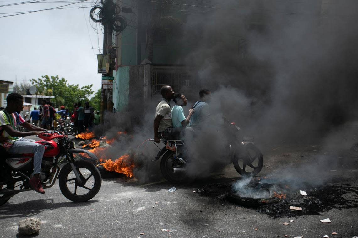 A motorcycle taxi driver carries clients past a burning barricade set by taxi drivers to protest the country’s fuel shortage in Port-au-Prince, Haiti, Wednesday, July 13, 2022.