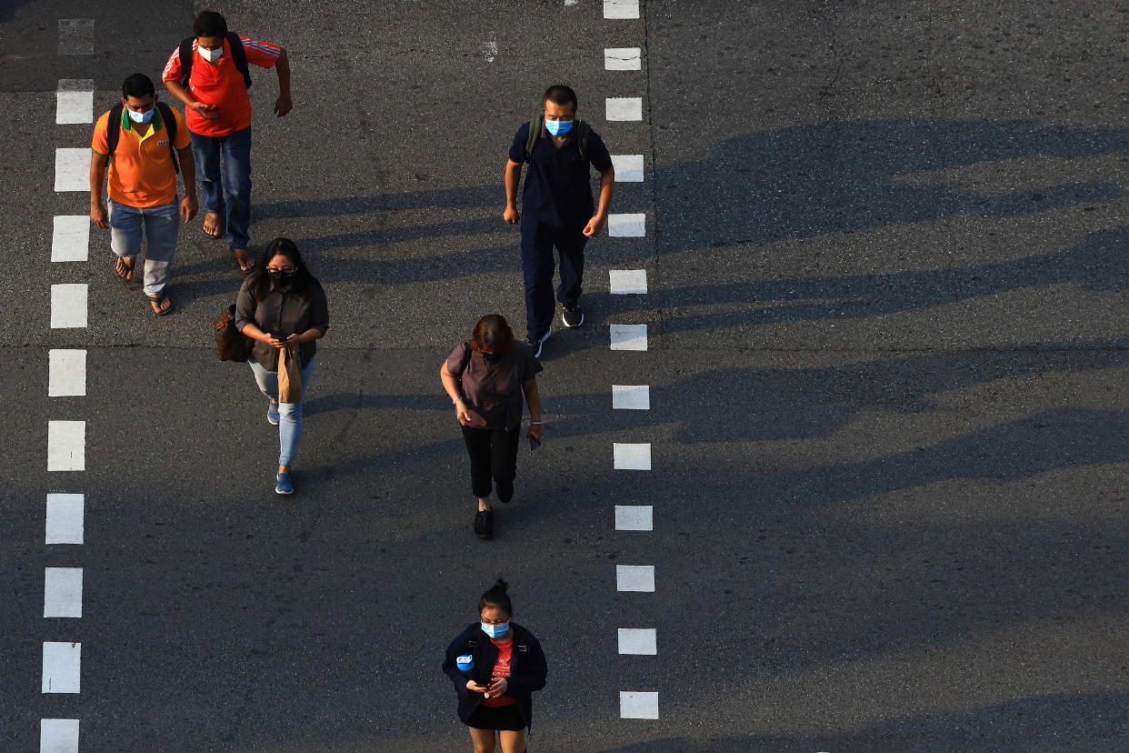 People wearing protective mask cross a street on June 8, 2021 in Singapore. Singapore enters a month long heightened alert from May 16 to June 13 to curb the spread of COVID-19 cases in the local community. New restrictions on movements and activities have been introduced such as limiting social interaction to two, prohibiting dining out and a reduced operating capacity at shopping malls, offices and attractions. (Photo by Suhaimi Abdullah/NurPhoto via Getty Images)