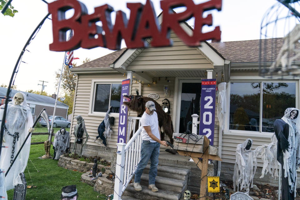 Trump supporter Terry Frandle checks his mailbox in his front yard decorated for Halloween and a Trump reelection campaign in Saint Clair Shores, Mich., Wednesday, Oct. 28, 2020. In Macomb County, Frandle hung Trump banners outside his house and noticed that neighbors who used to stop to chat crossed to the other side of the street, not even offering a "hello." Some drivers wave, some flip the bird. He doesn't blame Trump for the discord, he blames Democrats and the media for failing to give Trump a fair shake, he said. He plans to vote in person on Election Day. "I just don't trust anything anymore," he said, except for what he hears directly from Trump. (AP Photo/David Goldman)