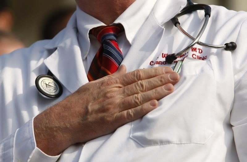 A doctor puts his hand over his chest during a