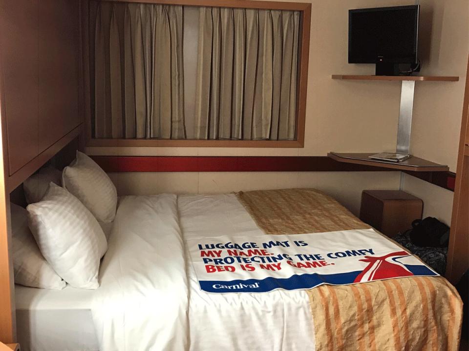 A stateroom on a carnival cruise with a large bed and window behind it