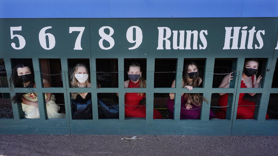 While wearing their prom gowns, students peer through the scoreboard at the New Hampshire Fisher Cats minor league baseball stadium in Manchester, N.H., on Monday, April 26, 2021. After a year without proms, school districts across the country are debating whether they can safely hold an event that many seniors consider a capstone to their high school experience. The nearly 300 student senior class of Manchester's Central High School are waiting to get approval from the city's board of health so they can have their prom at the outdoor venue, due to COVID-19 concerns. (AP Photo/Charles Krupa)