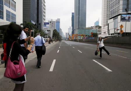 A woman takes a picture of her friend as Thamrin business district near the site of a bomb blast is seen empty in Jakarta, January 14, 2016. REUTERS/Beawiharta