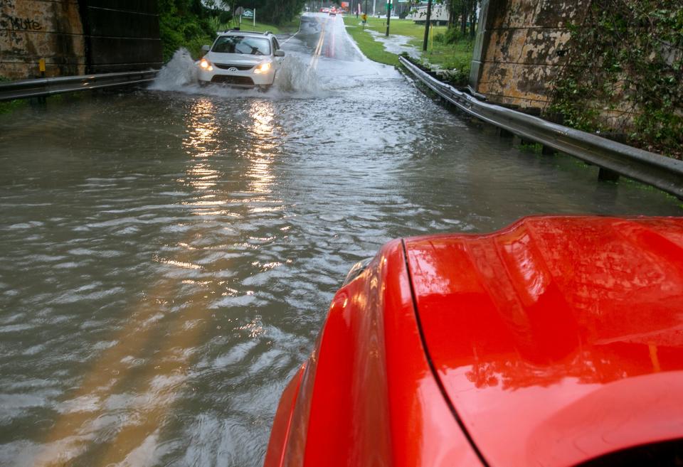 Cars navigate the flooded roadway under the train trestle at Southeast Third Avenue on Tuesday.