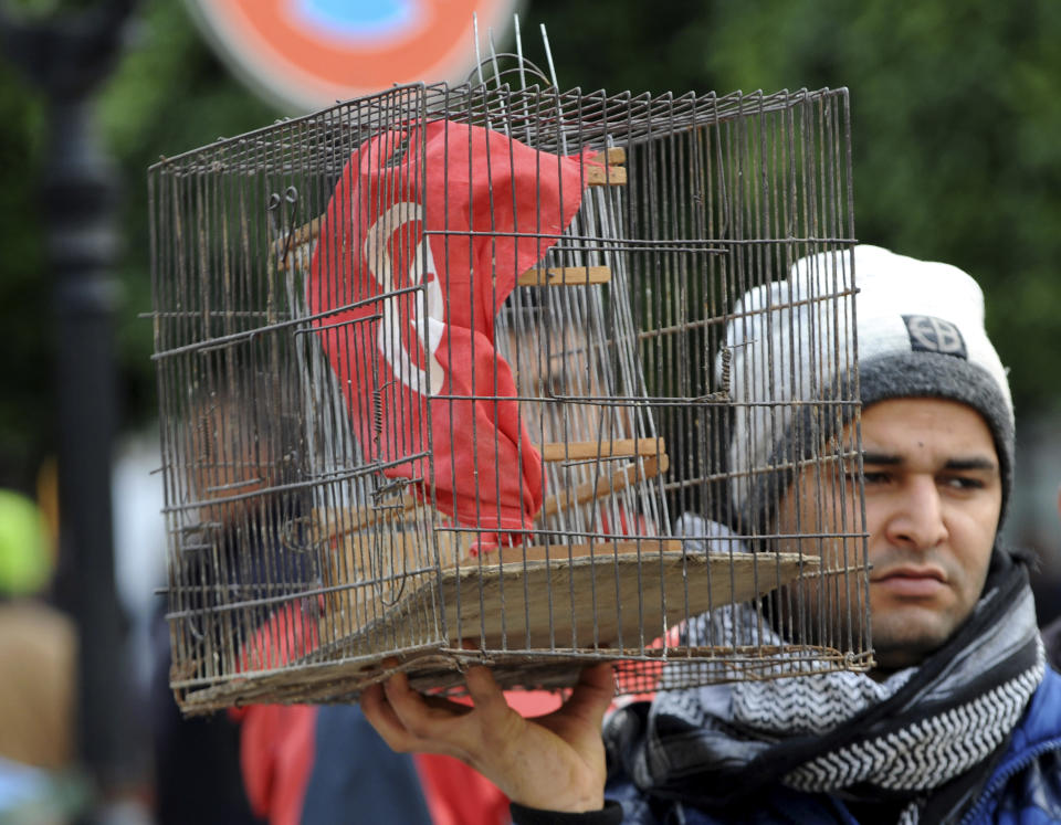 FILE - A Tunisian holds a bird cage countaining his national flag during a demonstration to mark the eighth anniversary of the democratic uprising in Tunis, Monday, Jan.14, 2019. Despite an election debacle, Tunisia's increasingly authoritarian president appears determined to upend the country's political system, threatening to unravel the fragile democracy and collapse the economy in the North African nation that a decade ago stood out as a model of good governance and economic prosperity in the aftermath of the Arab Spring protests. (AP Photo/Hassene Dridi, File)