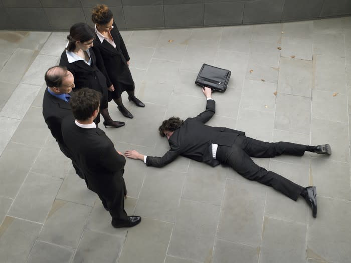 Four businesspeople looking down at a fallen colleague who isn't getting up