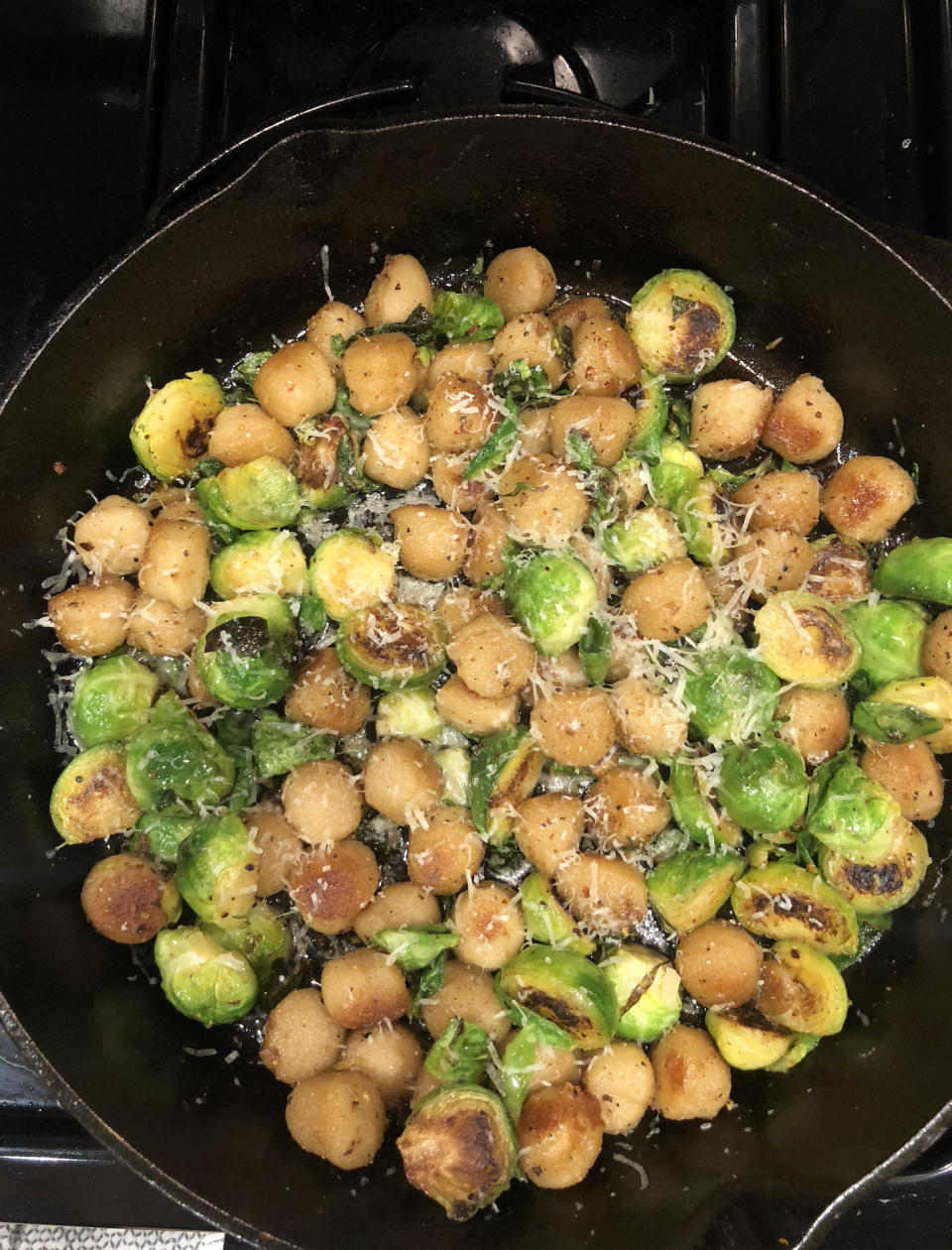 Sautéed Brussels sprouts and round potatoes in a pan, sprinkled with grated cheese