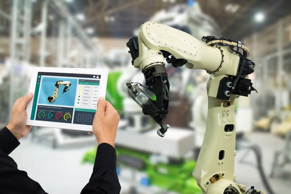 a man holding up a tablet to monitor a manufacturing robotic arm