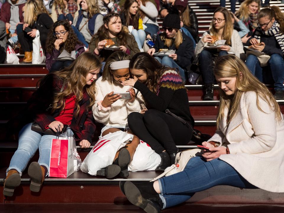 A group of teens look at a smartphone.