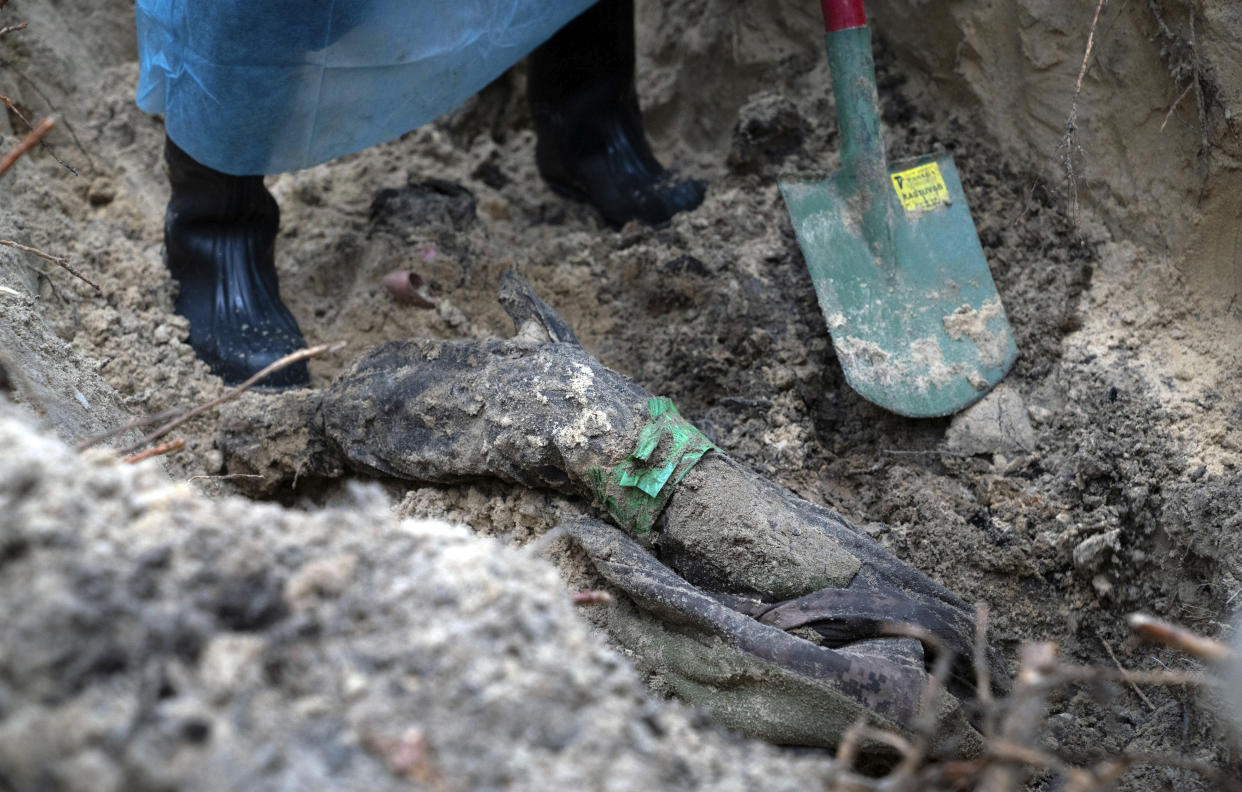 Part of the body of Ukrainian soldier emerges from the ground during an exhumation in the recently retaken area of Izium, Ukraine, Friday, Sept. 16, 2022. Ukrainian authorities discovered a mass burial site near the recaptured city of Izium that contained hundreds of graves. It was not clear who was buried in many of the plots or how all of them died, though witnesses and a Ukrainian investigator said some were shot and others were killed by artillery fire, mines or airstrikes. (AP Photo/Evgeniy Maloletka)