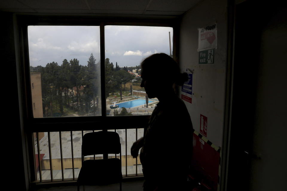 In this Friday, April 19, 2019, photo, a U.N female peacekeeper stands by a window with a view the pool of the Ledra Palace hotel inside the U.N. buffer zone in the divided capital Nicosia, Cyprus. This grand hotel still manages to hold onto a flicker of its old majesty despite the mortal shell craters and bullet holes scarring its sandstone facade. Amid war in the summer of 1974 that cleaved Cyprus along ethnic lines, United Nations peacekeepers took over the Ledra Palace Hotel and instantly turned it into an emblem of the east Mediterranean island nation's division. (AP Photo/Petros Karadjias)