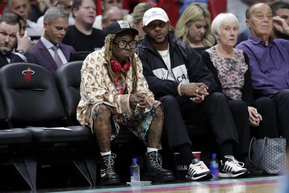 FILE - Rapper Lil Wayne, left, watches during the second half of an NBA basketball game between the Los Angeles Lakers and Miami Heat, Dec. 13, 2019, in Miami. Just as a movie soundtrack helps viewers follow the action of the narrative through each plot twist, hip-hop has done the same for basketball via the NBA. (AP Photo/Lynne Sladky, file)