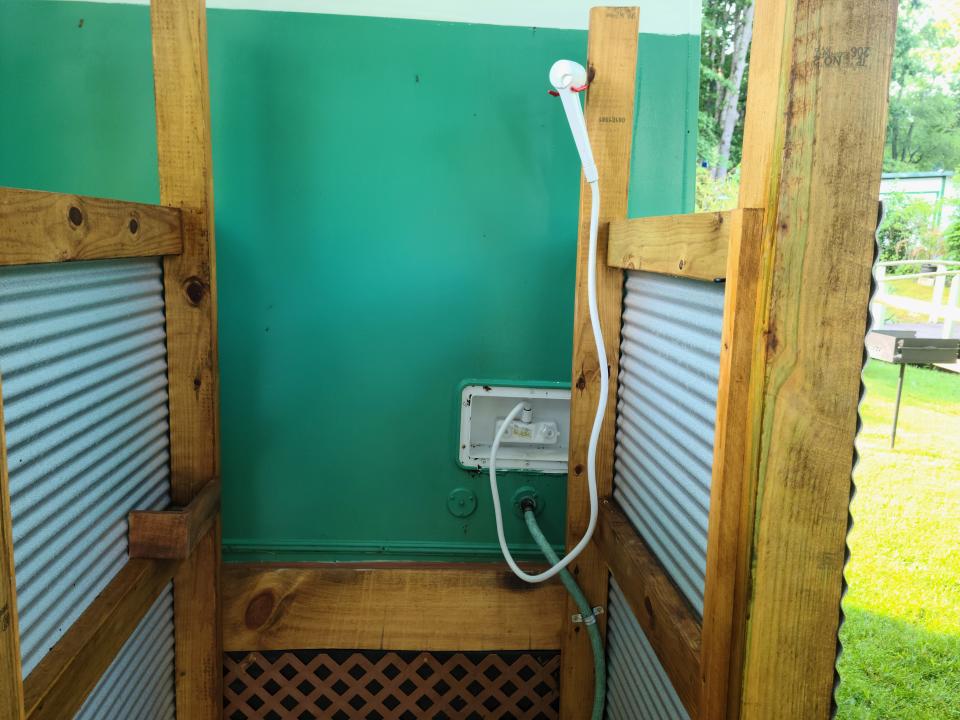 An outdoor shower with a white showerhead, green walls, and privacy screens.