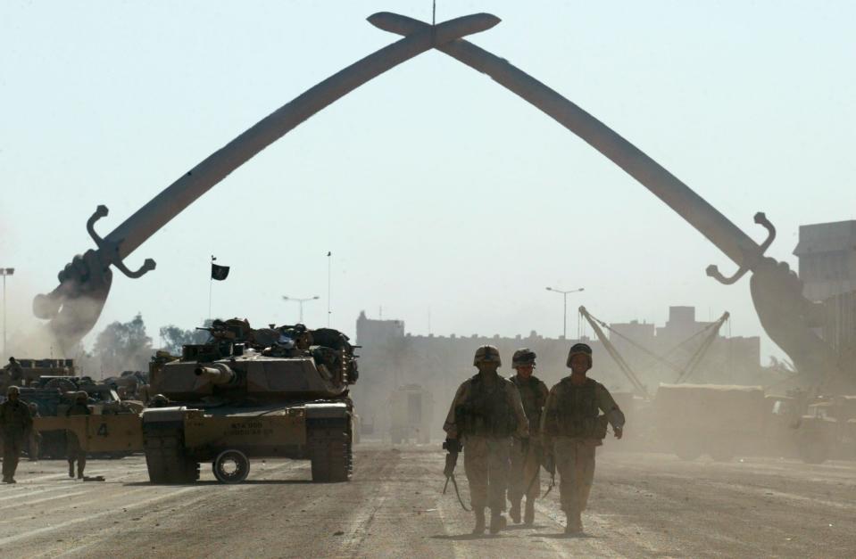 U.S. Army soldiers walk near a massive arch of swords at Saddam Hussein's military parade grounds Friday, April 11, 2003 — four days after the Thunder Run seized this ground from the Iraqi military. (AP Photo/John Moore)