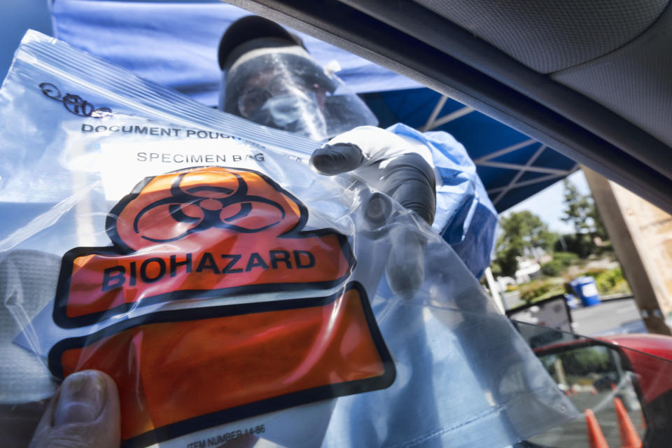 In this Wednesday, May 6, 2020 photo a medical worker hands a self administered coronavirus test to a patient at a drive through testing site in a parking lot in the Woodland Hills section of Los Angeles. The city of Los Angeles is providing free coronavirus tests to anyone who wants one regardless of whether they have symptoms. The offer reflects a parting with state guidelines after the mayor partnered with a startup testing company. The test the city is offering is easier to administer and doesn't require the scarce supplies that have created bottlenecks for expanded testing across California. (AP Photo/Richard Vogel)