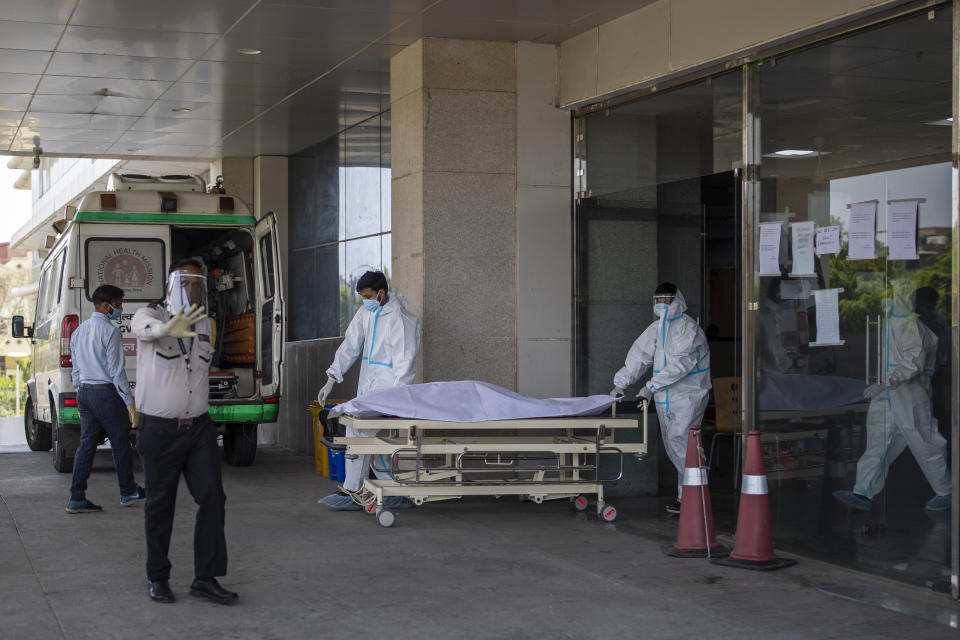 FILE - In this April 21, 2021, file photo, security guard objects to taking taking pictures as hospital staff shift the body of a COVID-19 patient on a stretcher to a waiting ambulance at a government COVID-19 hospital in Noida, a suburb of New Delhi, India. India is battling the world’s fastest pace of spreading infections. Its government has blocked vaccine exports for several months to better meet needs at home, exacerbating the difficulty of poor countries to access vaccine. (AP Photo/Altaf Qadri, File)