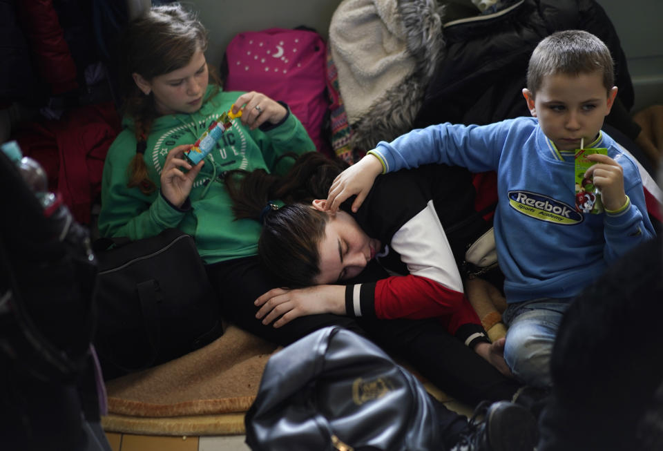 A woman and two children, who have fled Ukraine, take rest in the lobby of the train station in Przemysl, Poland, Sunday, March 13, 2022. Now in its third week, the war has forced more than 2.5 million people to flee Ukraine. (AP Photo/Daniel Cole)
