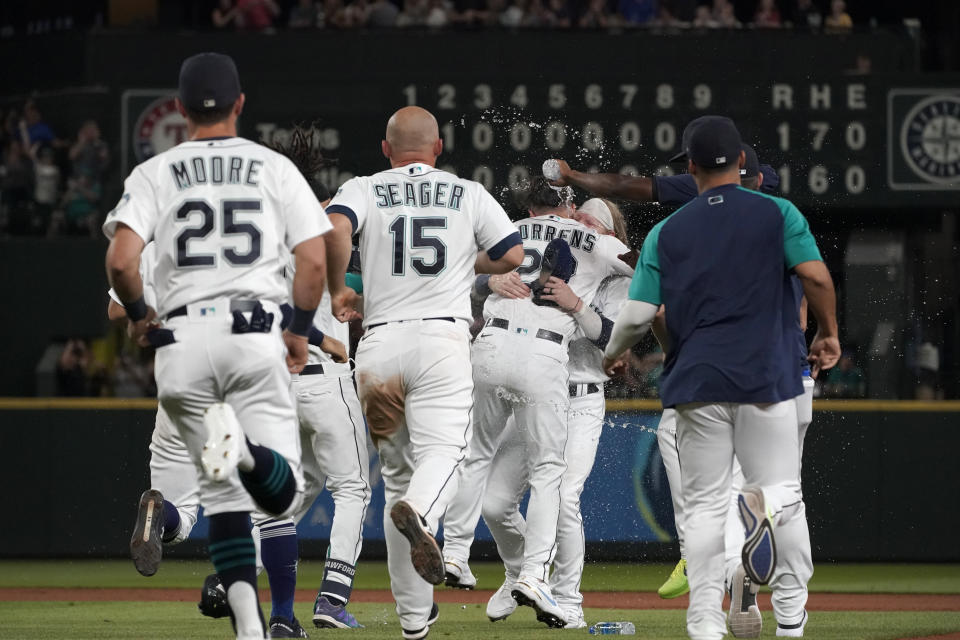 Seattle Mariners' Luis Torrens, center, is mobbed by teammates after he hit a single to score Jarred Kelenic with the winning run during the ninth inning of the team's baseball game against the Texas Rangers, Wednesday, Aug. 11, 2021, in Seattle. The Mariners won 2-1. (AP Photo/Ted S. Warren)