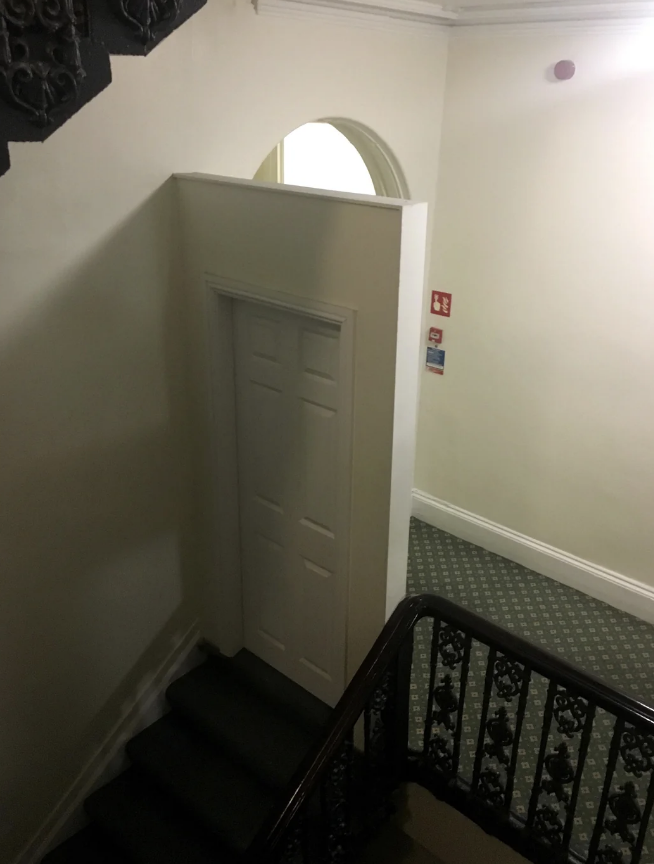 Interior staircase with a closed white door on a landing and ornate railing. No people are present